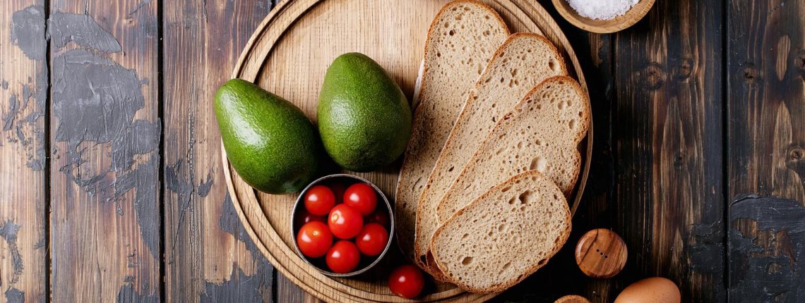 Ingredients for making avacado toast: bread, cherry tomatoes, avacado, eggs, olive oil and salt over dark wooden background. Top view, flat lay