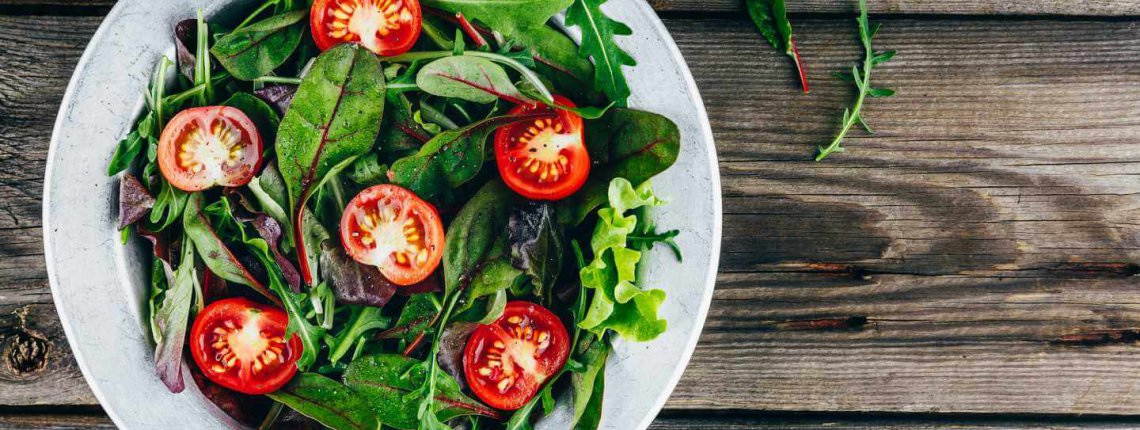 Mix of fresh green salad leaves with arugula, lettuce, spinach, beets and tomatoes on wooden rustic background. Top view.