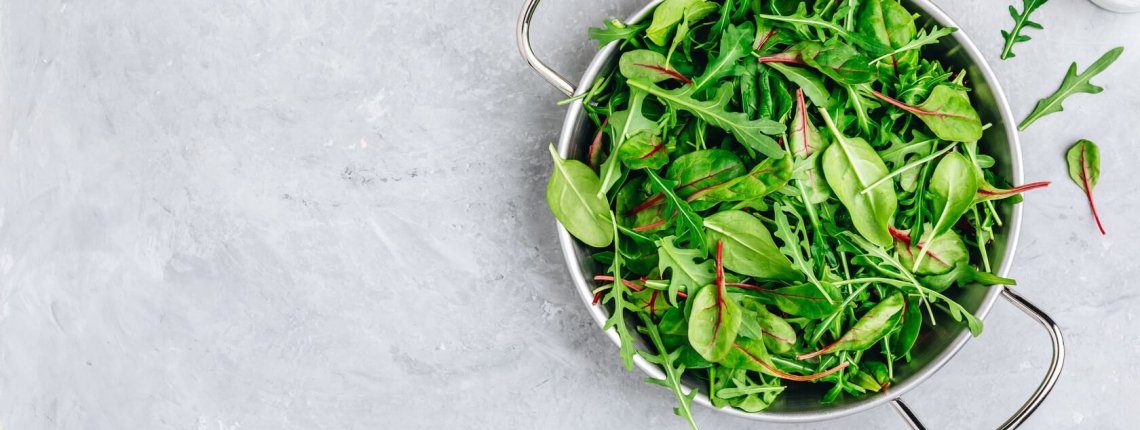 Mix of spring fresh leaves with arugula, lettuce, spinach, beets. Ingredients for salad on a gray stone background.