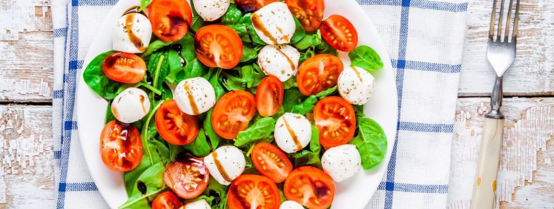 salad of mozzarella, cherry tomatoes and spinach with balsamic sauce on a white rustic table