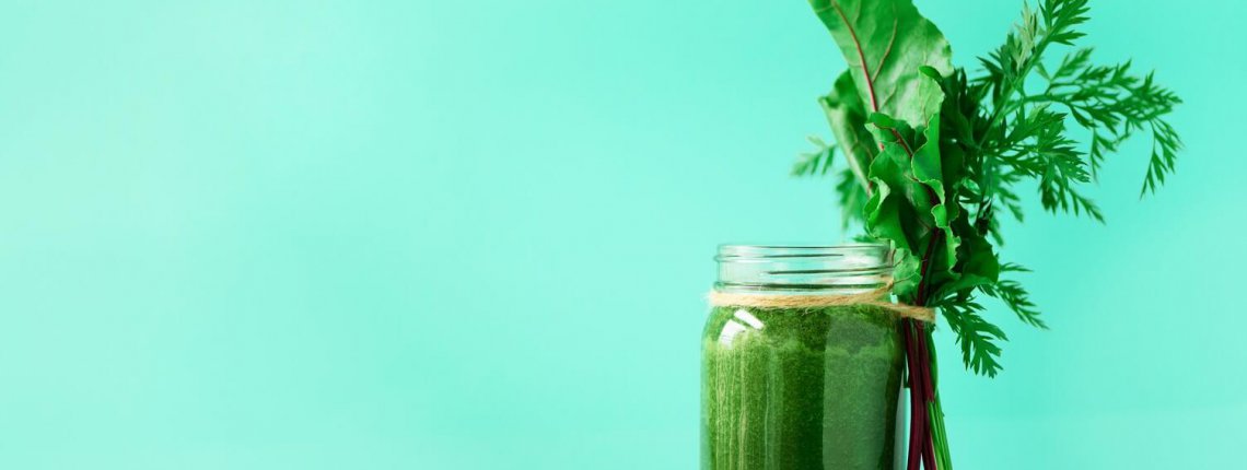 Smoothie with beet greens and carrot tops on blue background, copy space. Summer vegan food concept. Healthy detox eating, alkaline diet. Fresh squeezed juice, drink from vegetables. Leafy greens