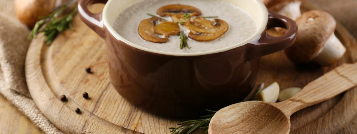 Composition with mushroom soup in pot, fresh and dried mushrooms, on wooden table, on sackcloth background